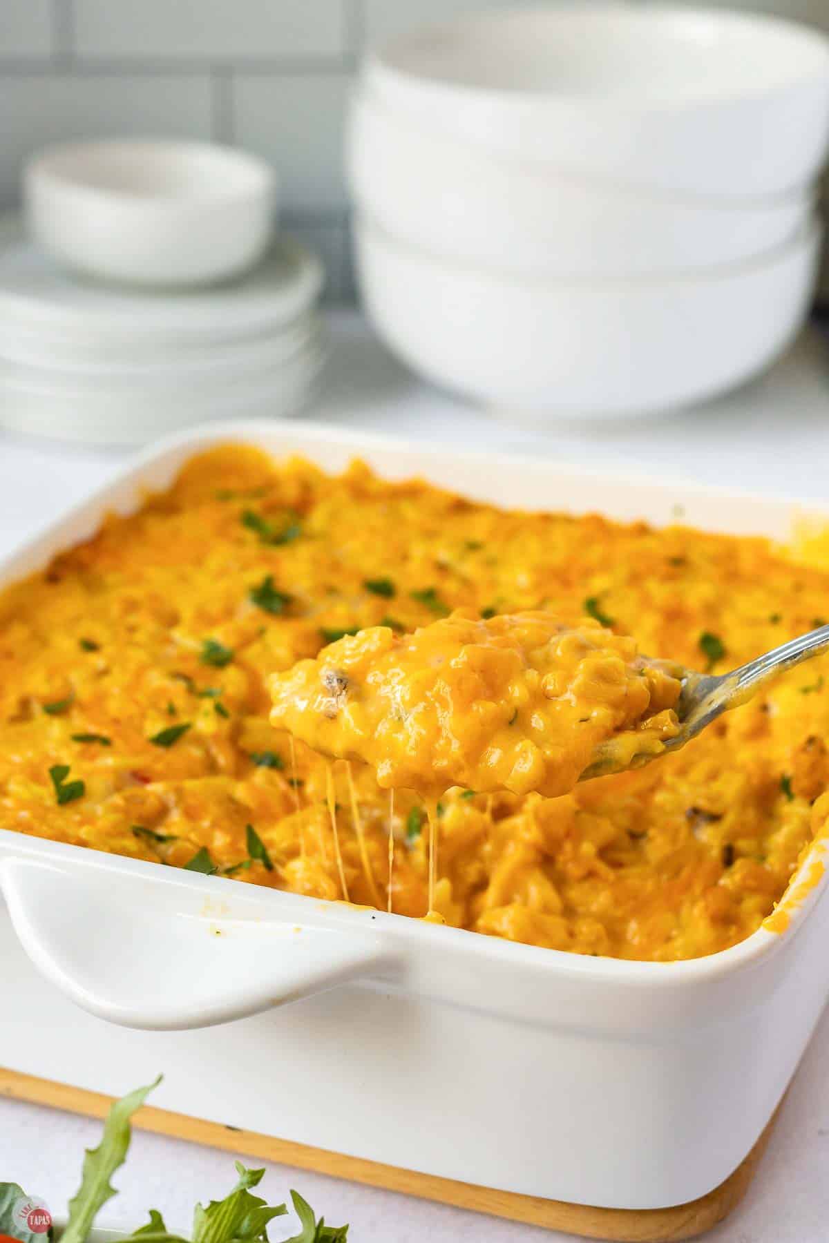Spoon lifting a cheesy scoop of yellow rice and corn casserole out of the baking dish