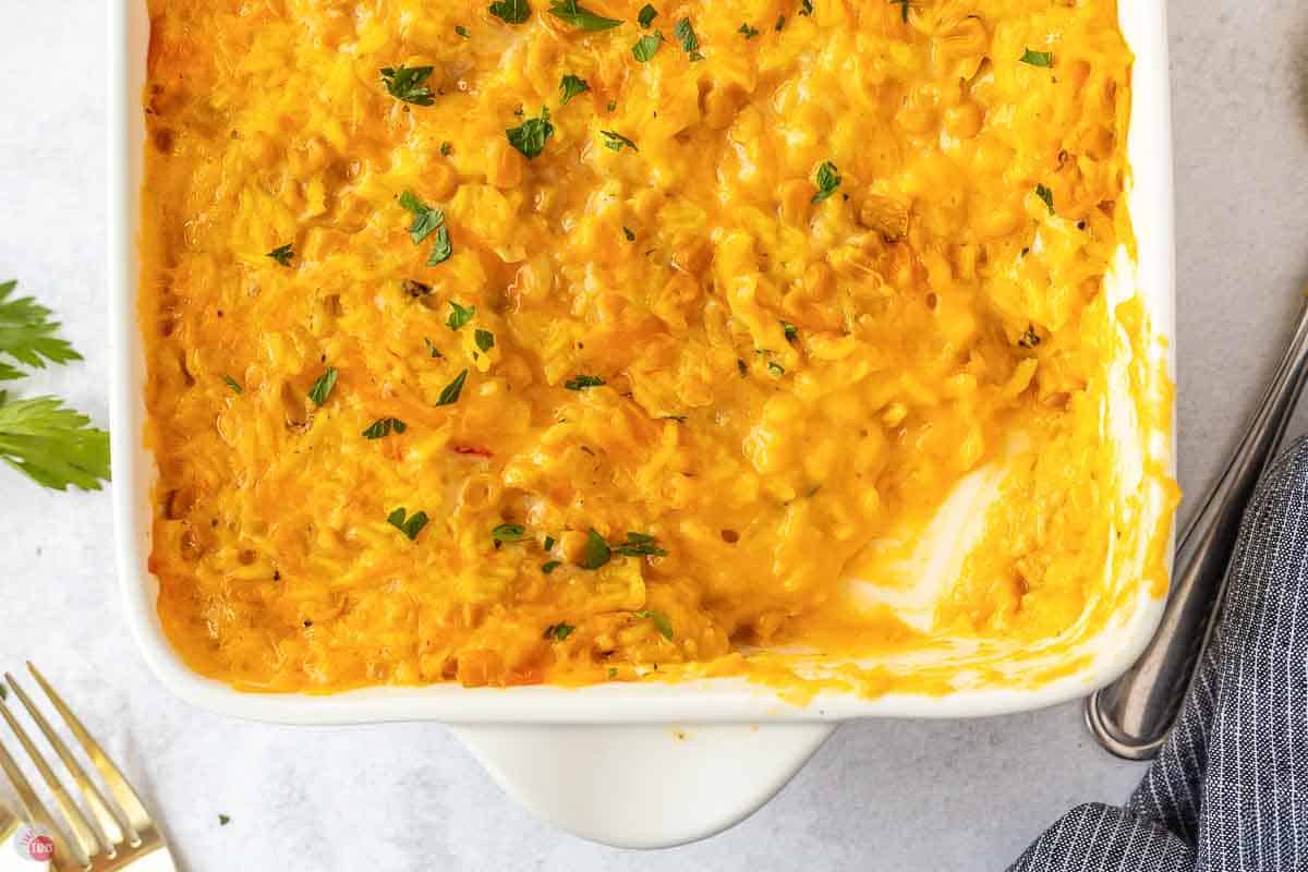 Cheesy corn and rice casserole in a white square baking dish with one scoop missing, topped with chopped parsley