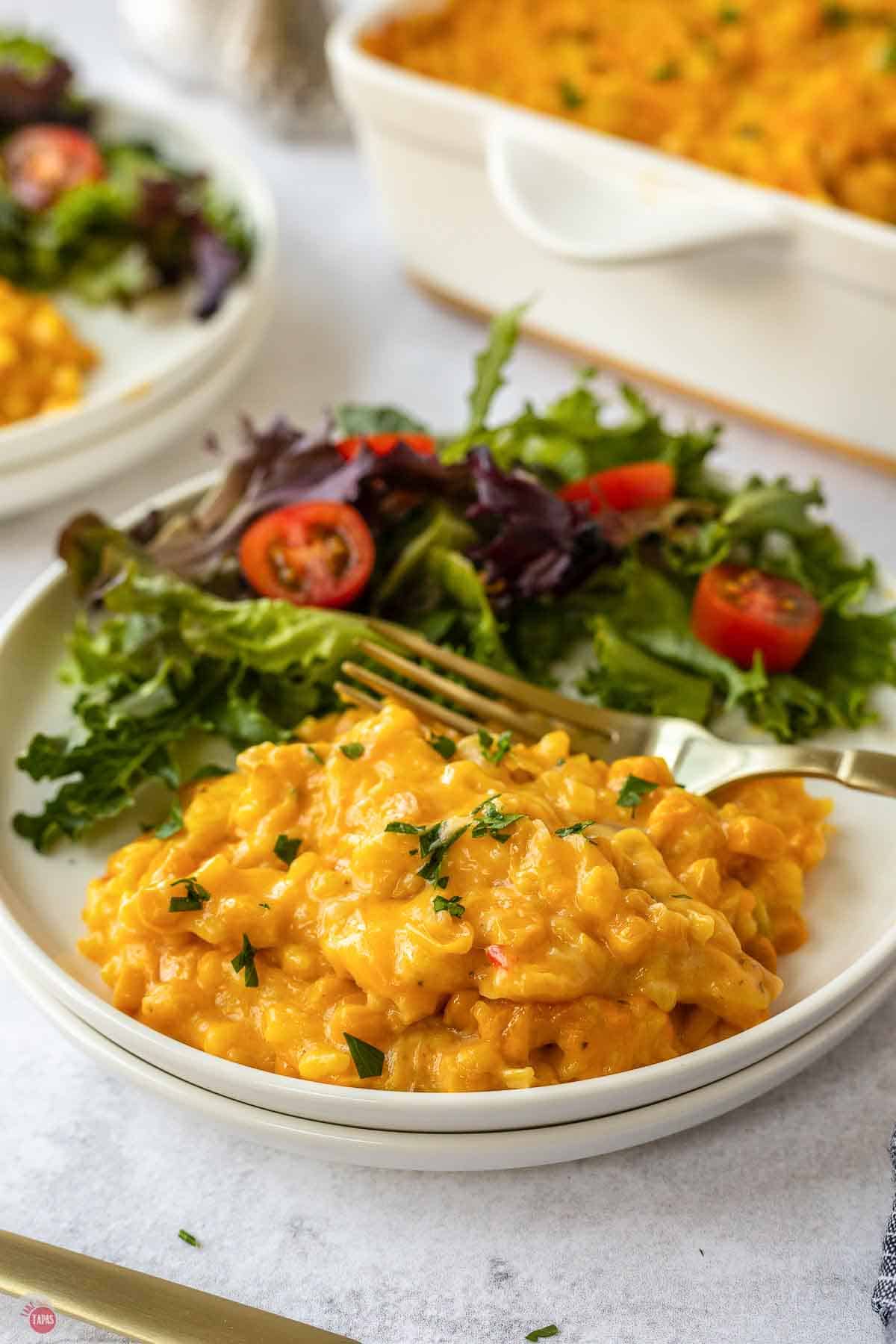 Plate of cheesy corn and rice casserole next to a salad with cherry tomatoes
