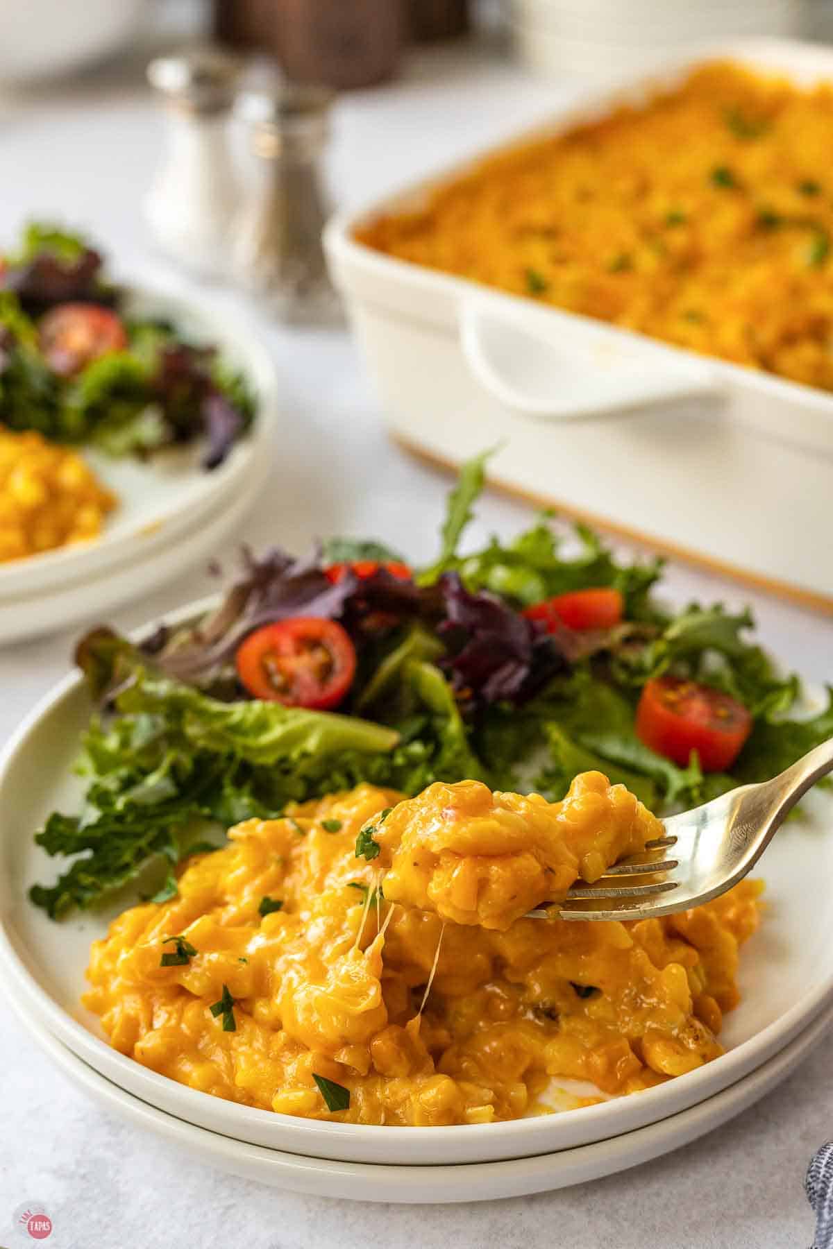 Fork lifting a bite of corn and rice casserole from a plate with a green salad