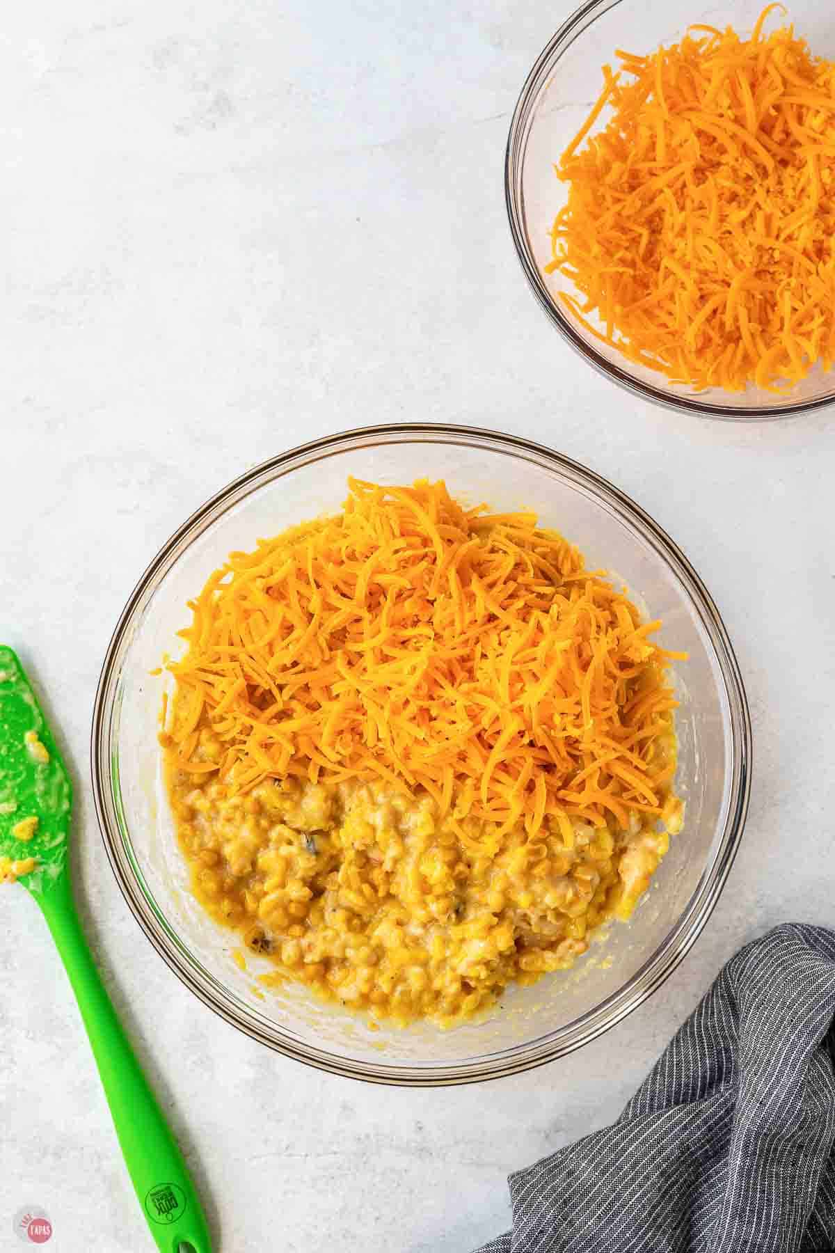 Shredded cheddar cheese piled on the corn and rice mixture in a glass bowl