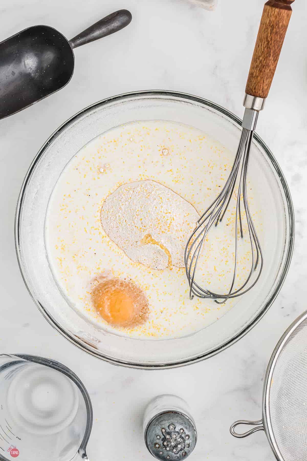 clear mixing bowl with a whisk mixing eggs and milk