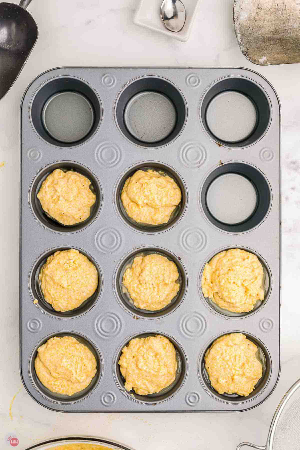 muffin pan with batter being scooped into each cup