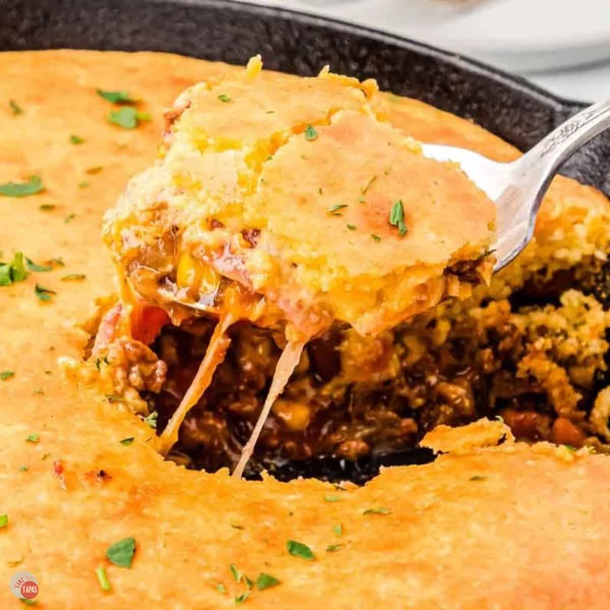 cast iron skillet with a spoon scooping out some casserole