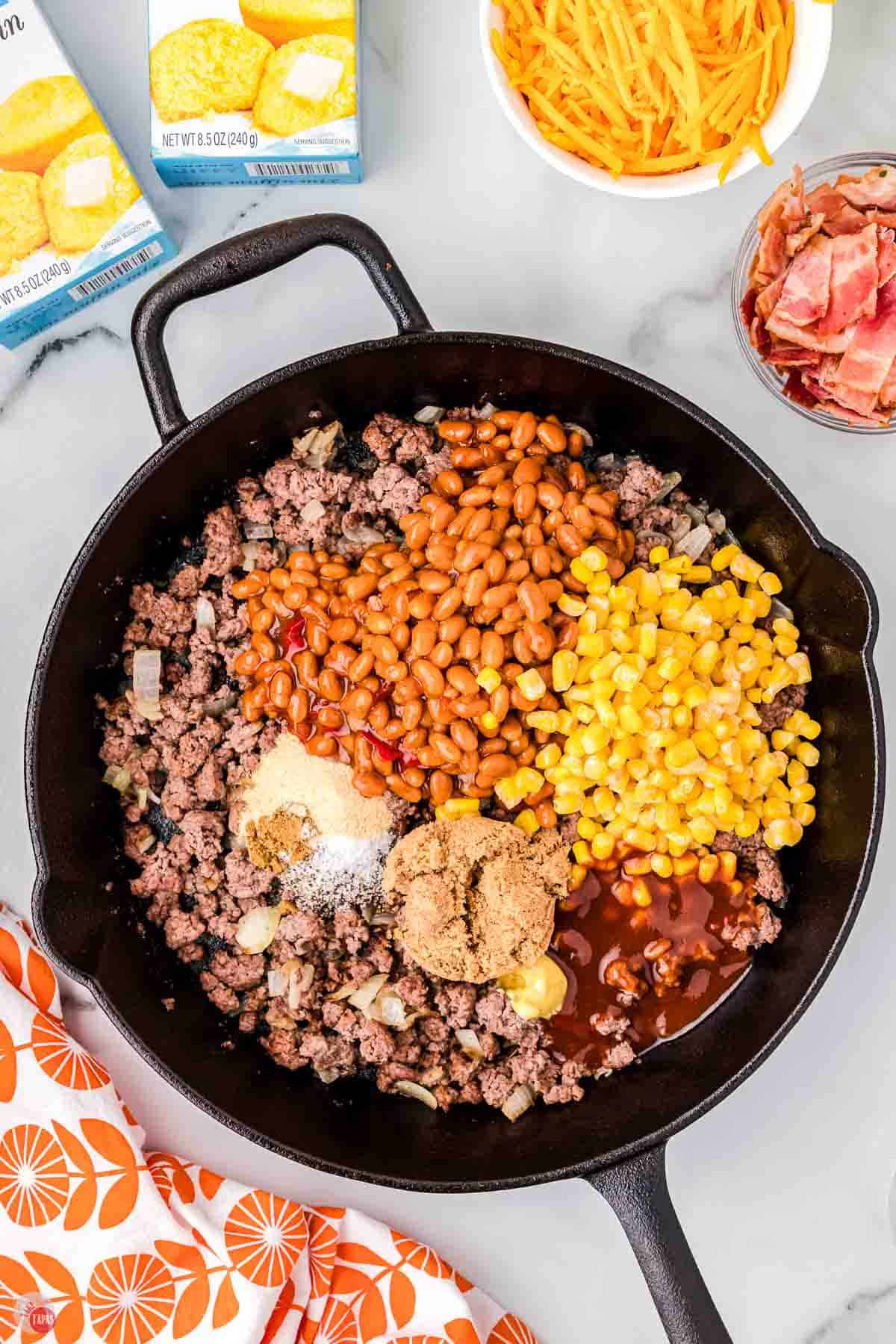 cast iron skillet with cooked ground beef, beans, corn, and spices