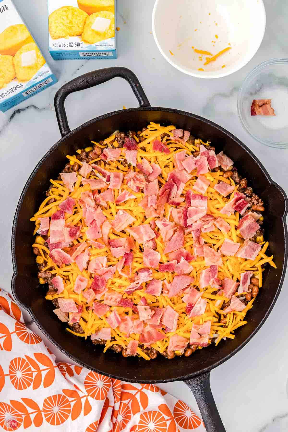iron skillet with ground beef mixture topped with shredded cheese and pieces of bacon
