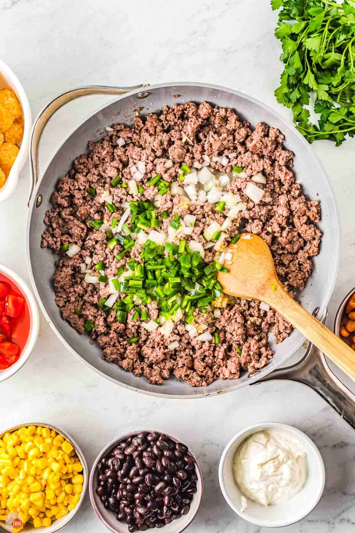 ground beef and onions cooking in a skillet with a wood spoon