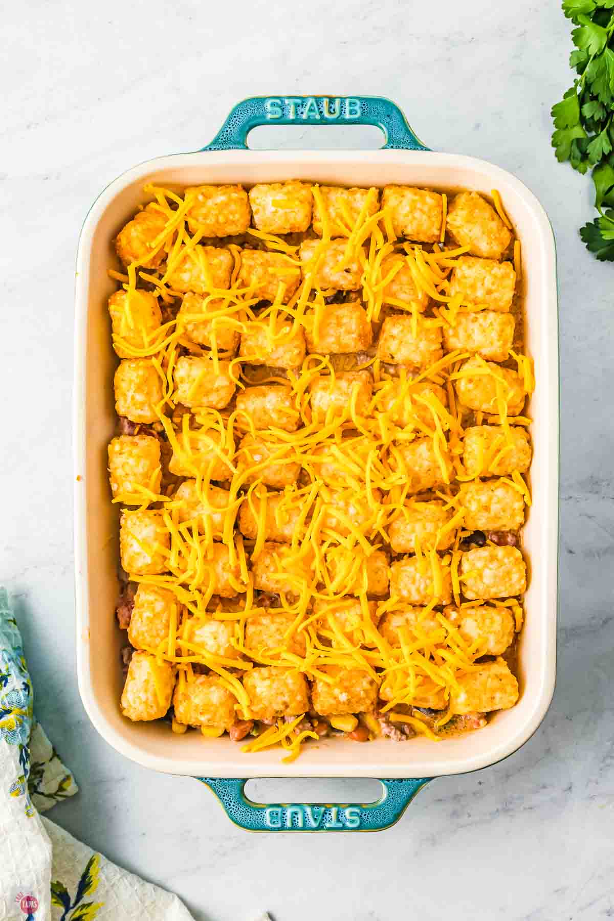 baking dish with cowboy casserole topped with tater tots and shredded cheese before baking
