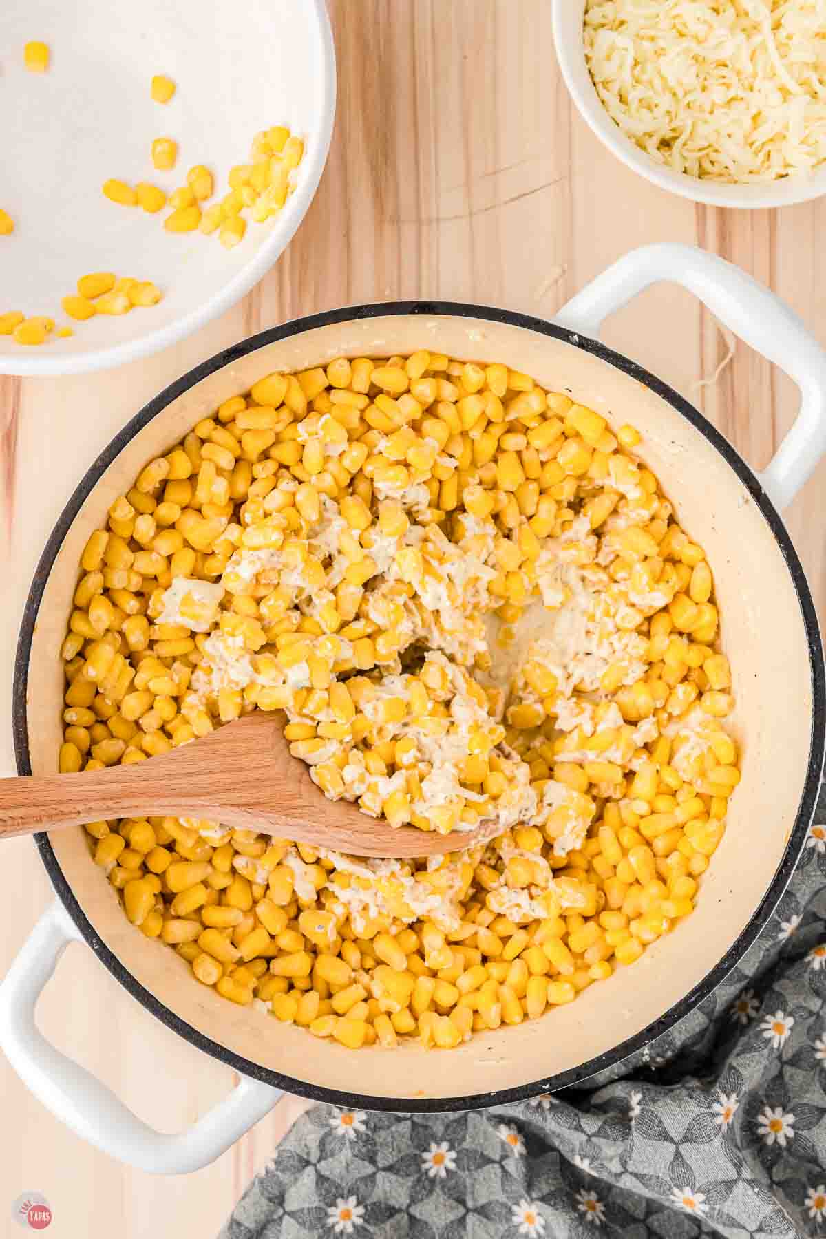white pot with a wood spoon stirring corn and a cheese sauce