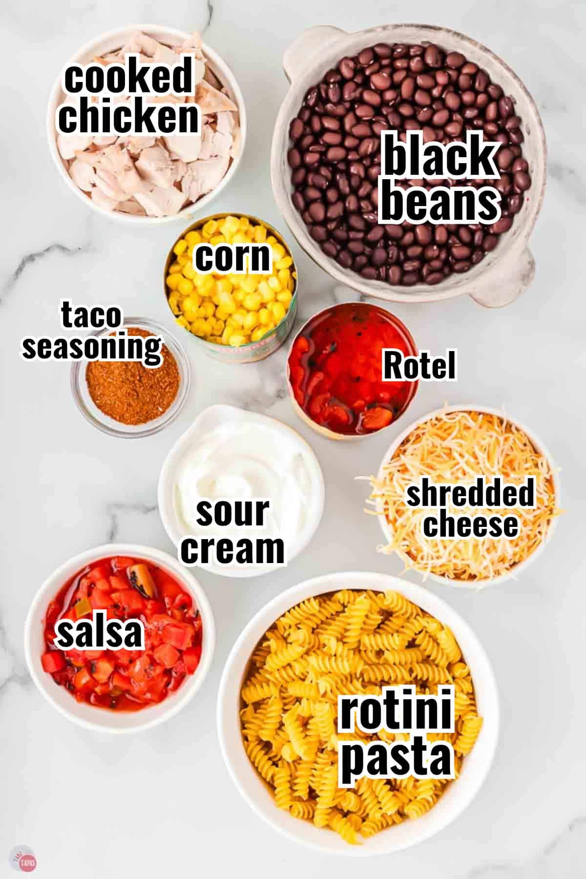 Fiesta chicken casserole ingredients in labeled bowls, including chicken, black beans, corn, Rotel, salsa, sour cream, taco seasoning, cheese and rotini