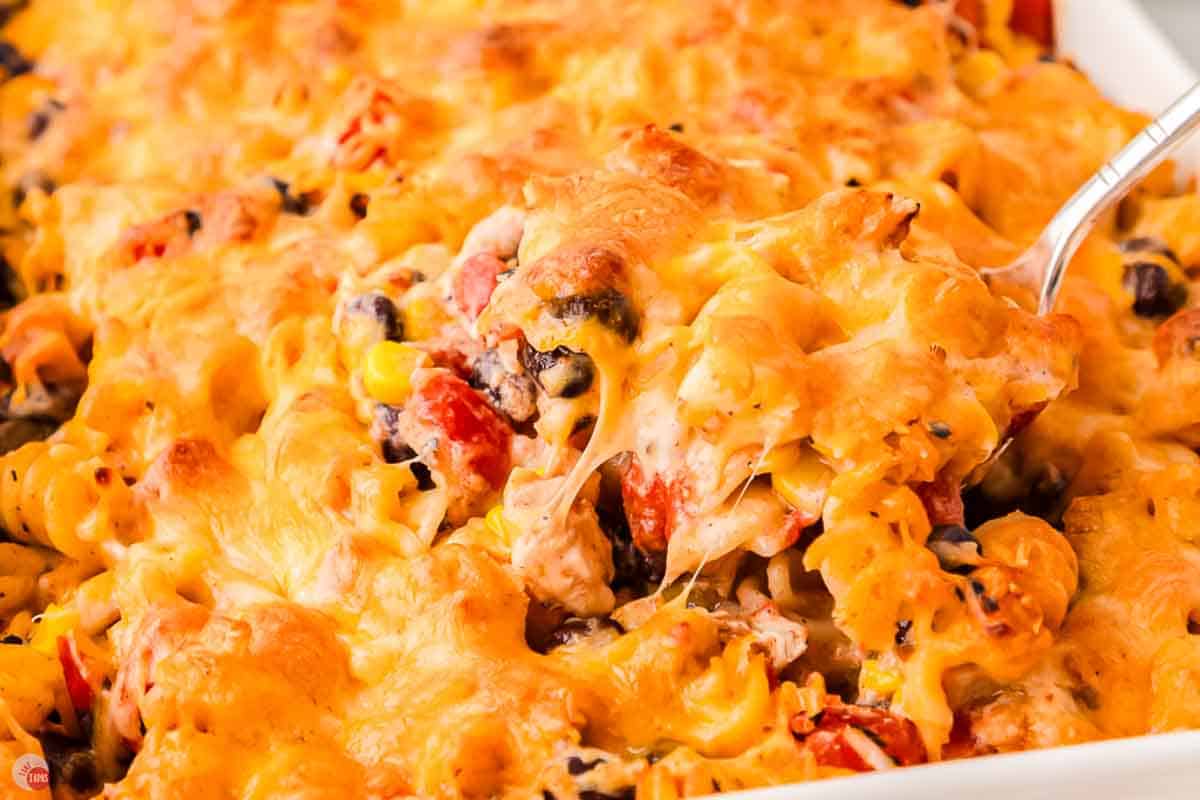 Spoon lifting a cheesy scoop of fiesta chicken casserole out of a white baking dish
