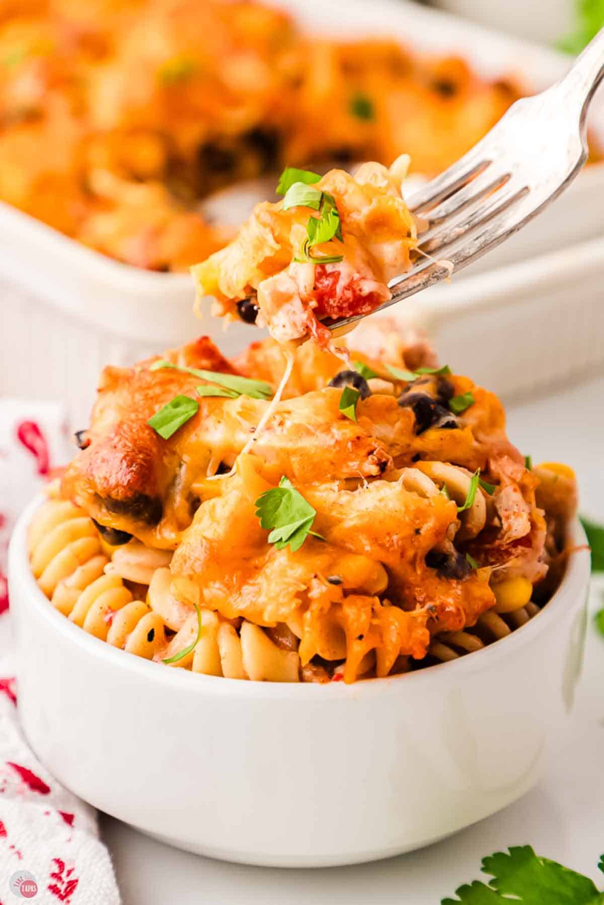 Fork lifting a bite of fiesta chicken casserole from a white bowl
