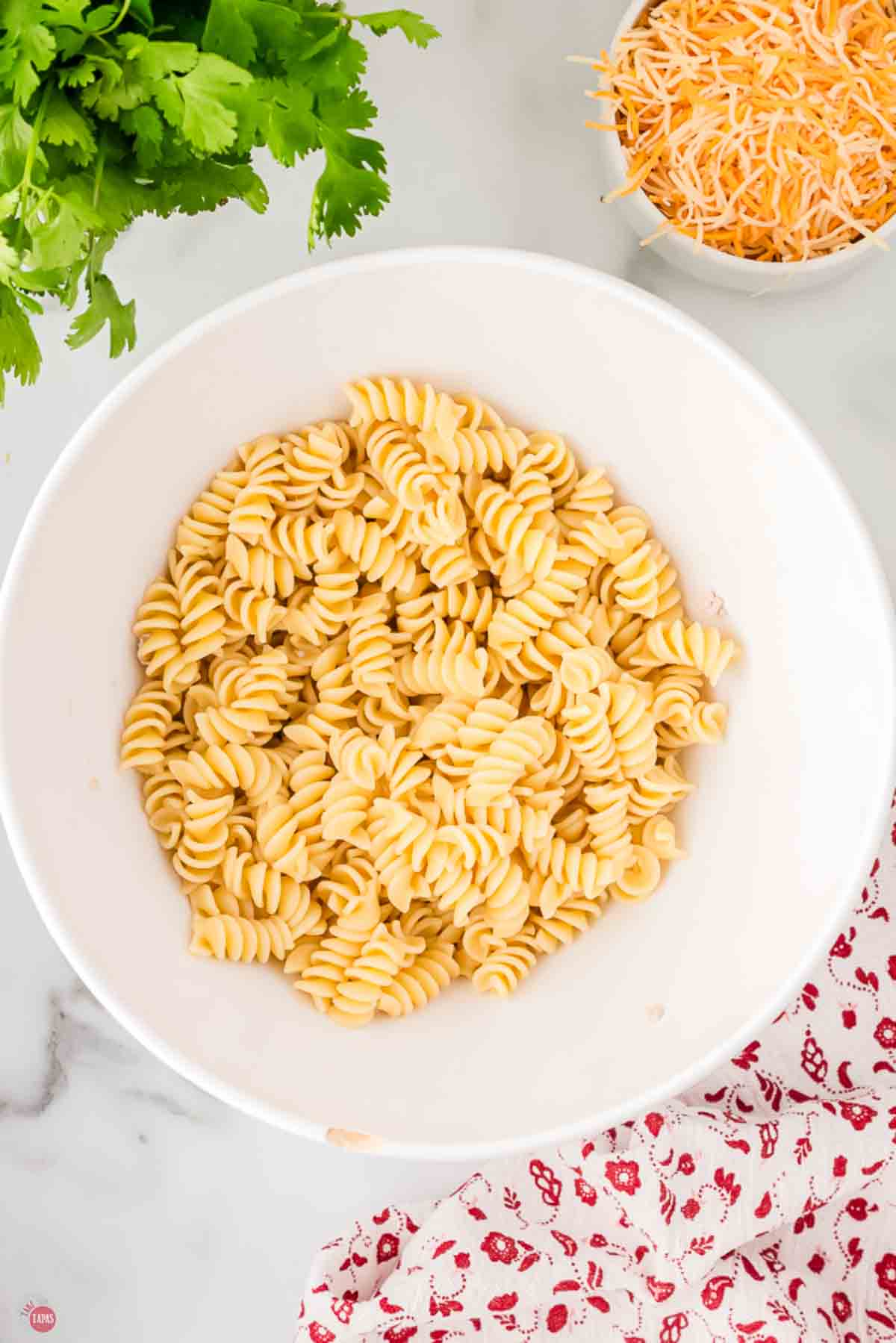 Cooked rotini pasta in a large white mixing bowl