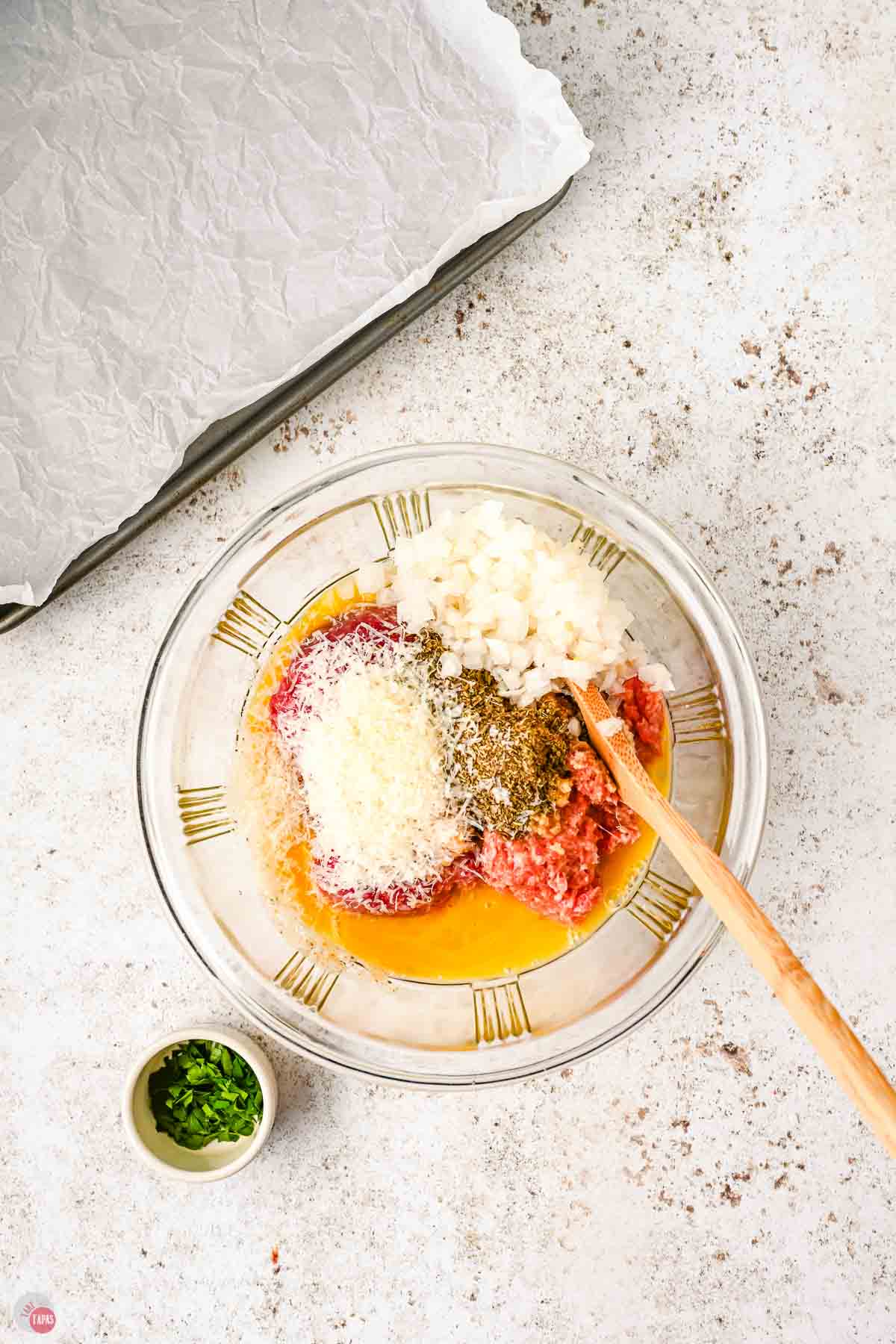 clear bowl with ground beef, spices, and cheese being mixed together