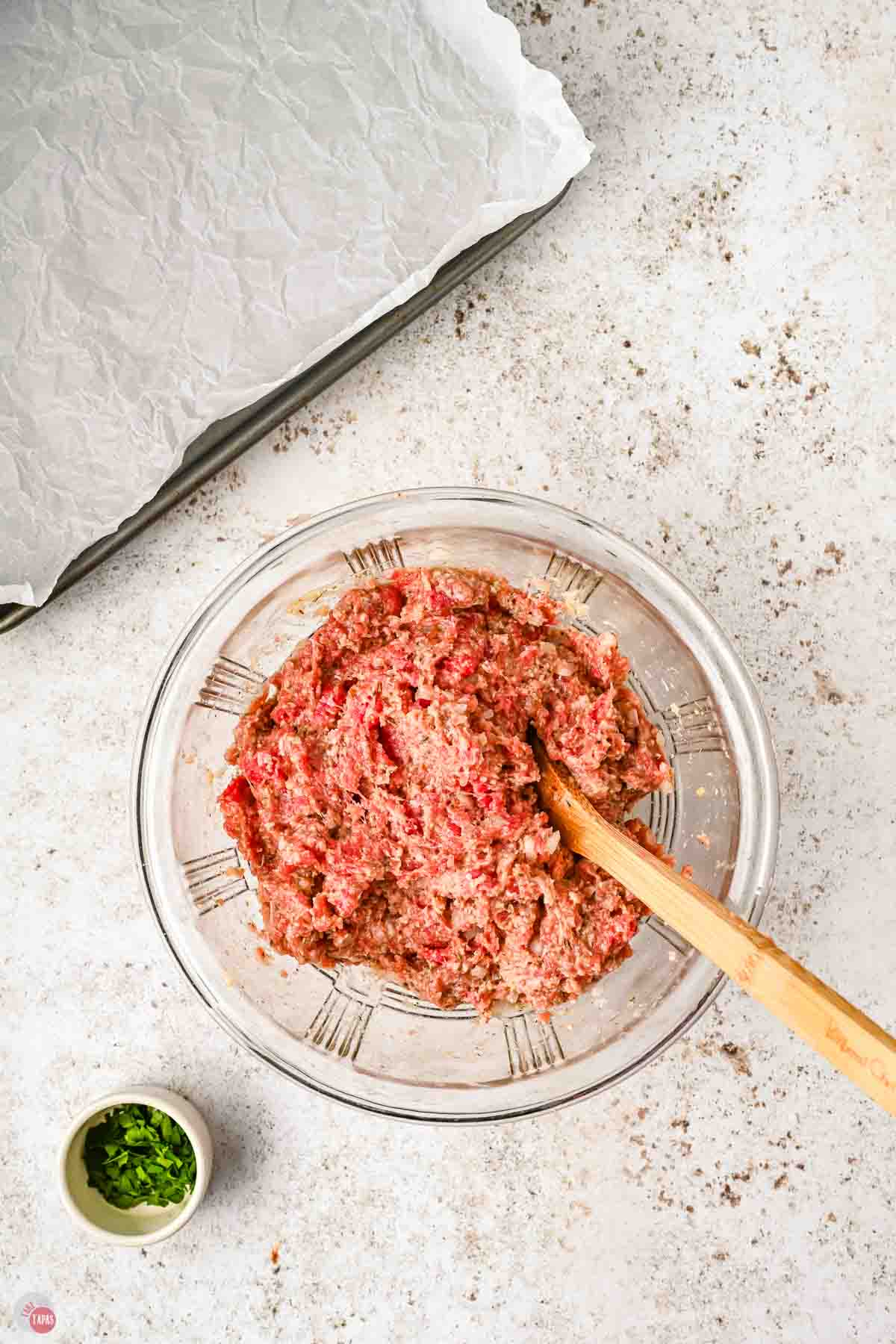 meatball meat mixture in a clear bowl with a spoon