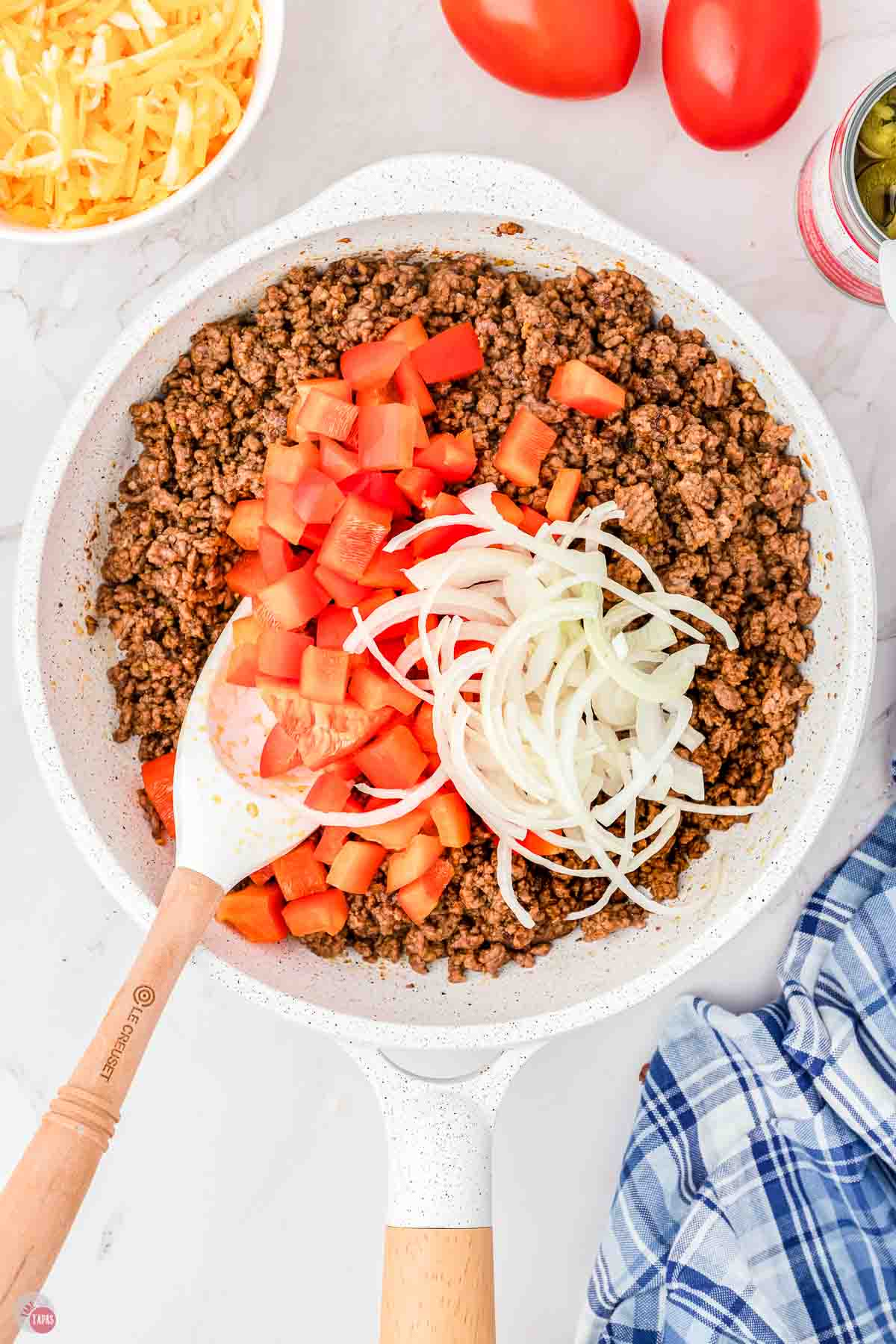 cooked ground beef in a skillet topped with bell peppers and sliced onions