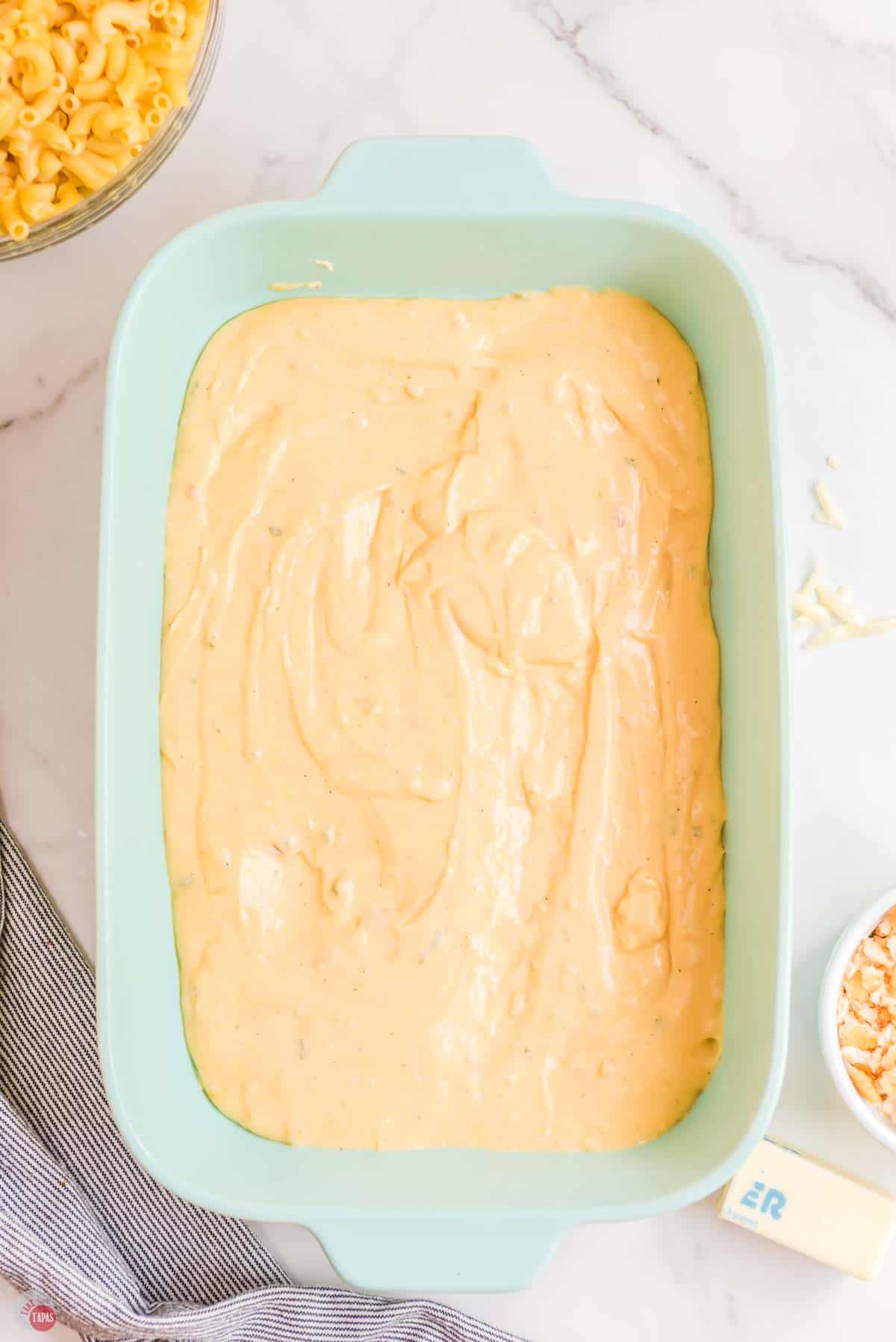 cheese sauce spread in the bottom of a green baking dish