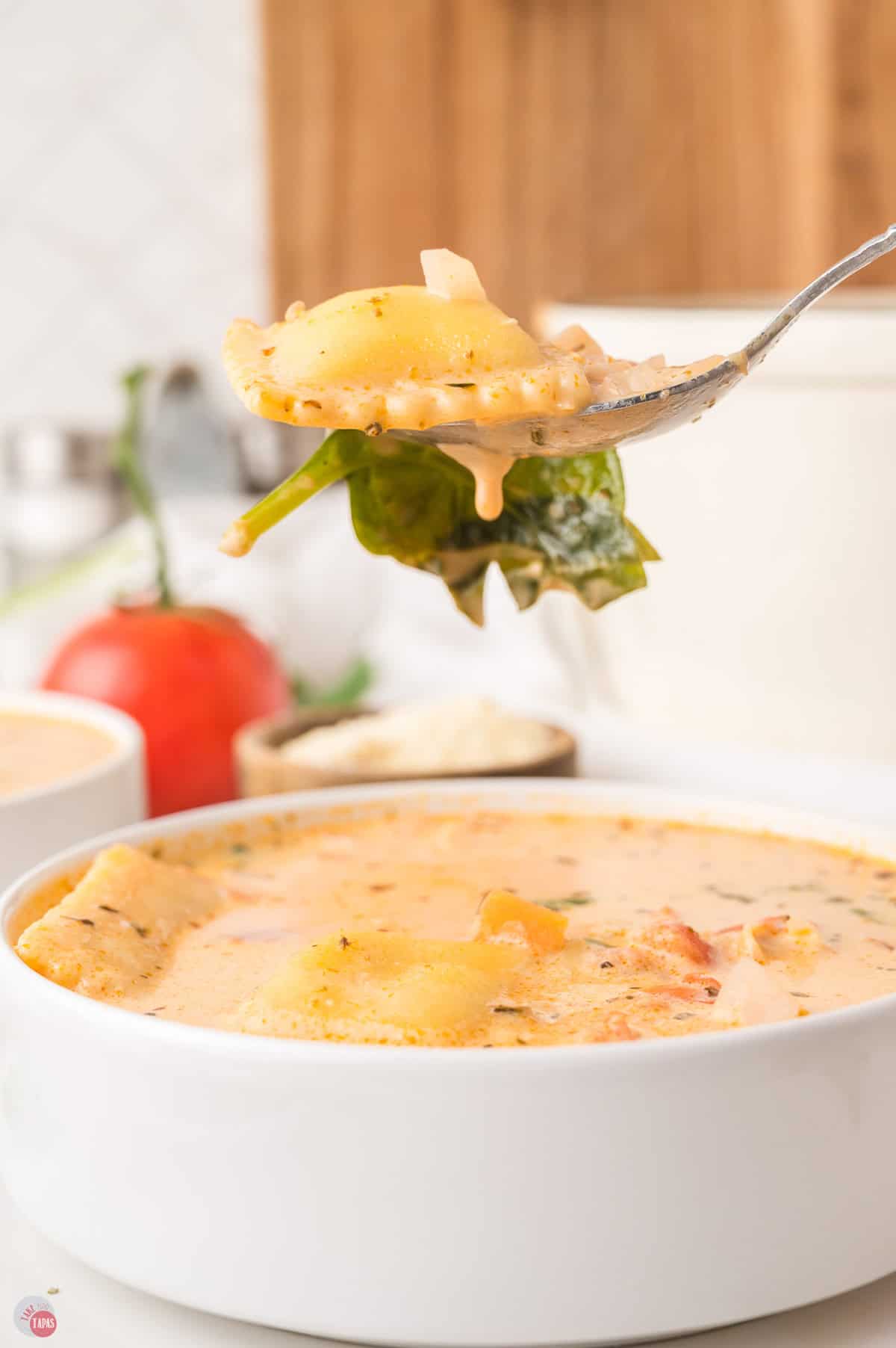 Spoon lifting a cheese ravioli and wilted spinach out of a bowl of creamy ravioli soup