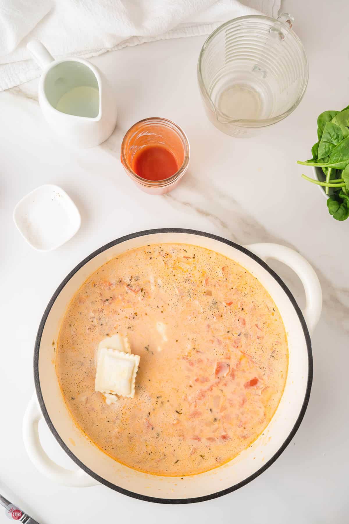 Frozen cheese ravioli going into the boiling creamy tomato soup in a white Dutch oven