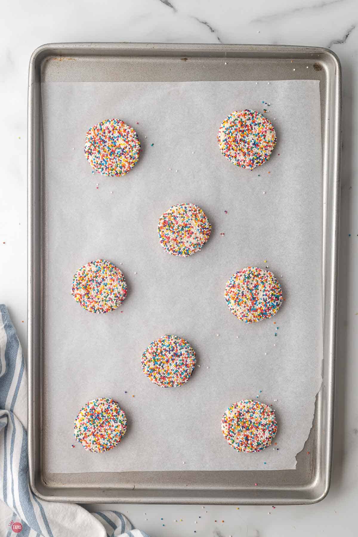 cookie dough discs covered in sprinkles on a parchment lined baking sheet